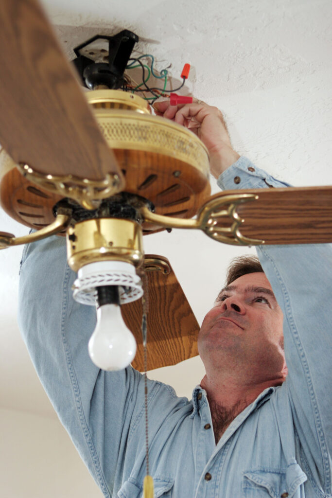 An electrician disconnecting the wires of an old ceiling fan.